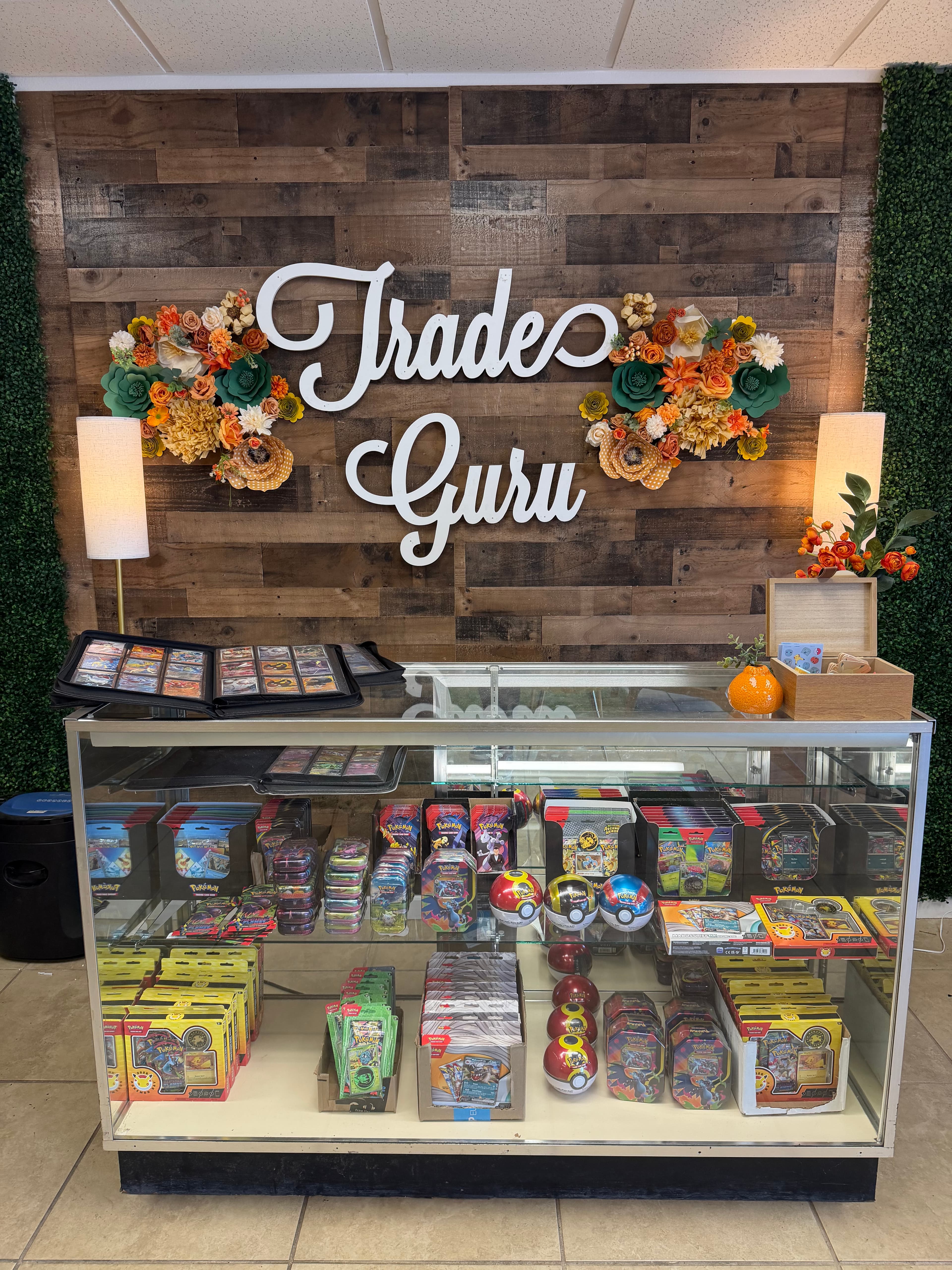 Trade Guru retail display with a floral wooden wall and glass case of Pokémon cards.