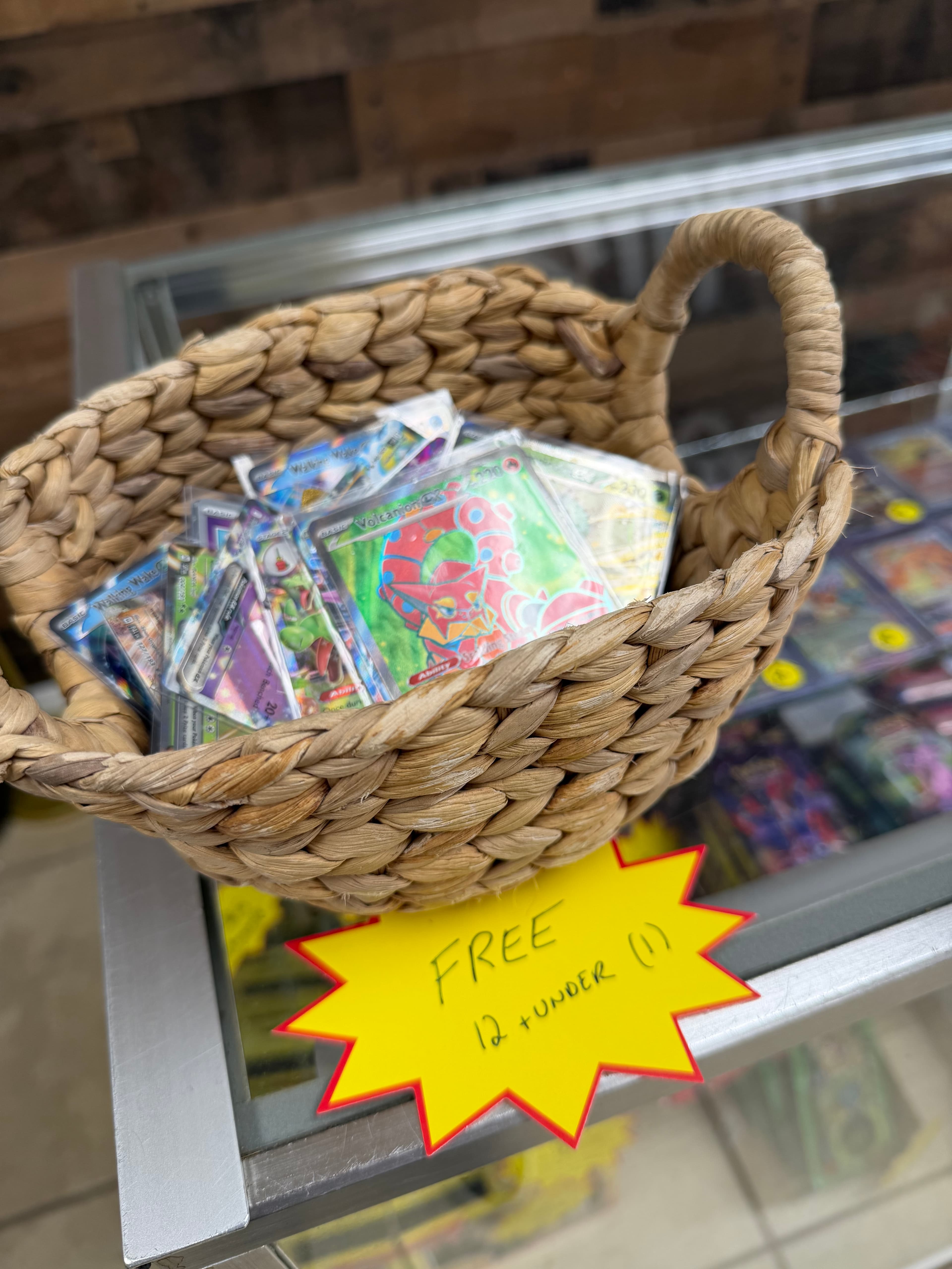 Woven basket of Pokémon cards on a glass counter with a yellow "FREE" sign.