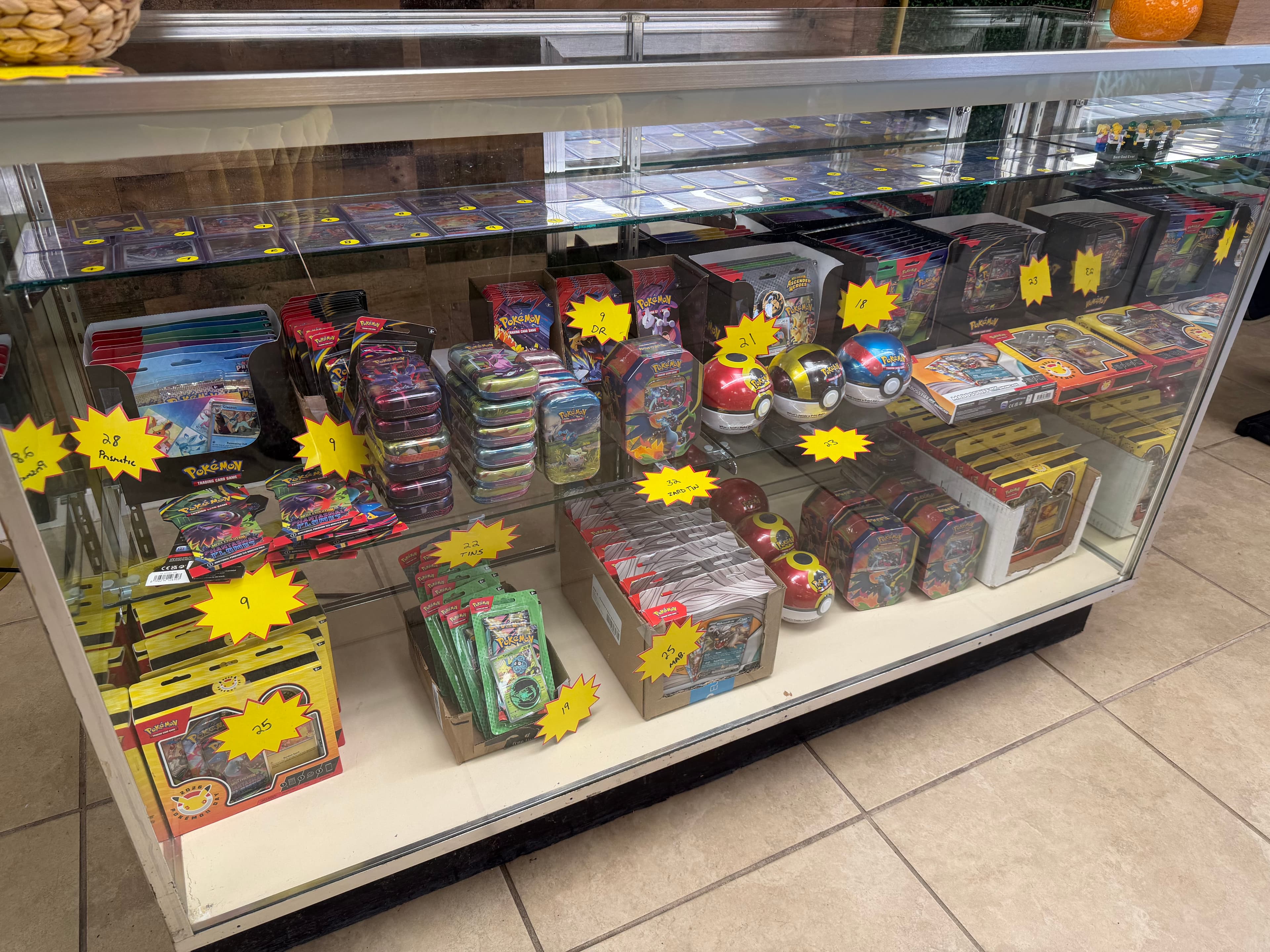 Glass display case filled with Pokémon trading card game booster packs, tins, and Poké Balls.