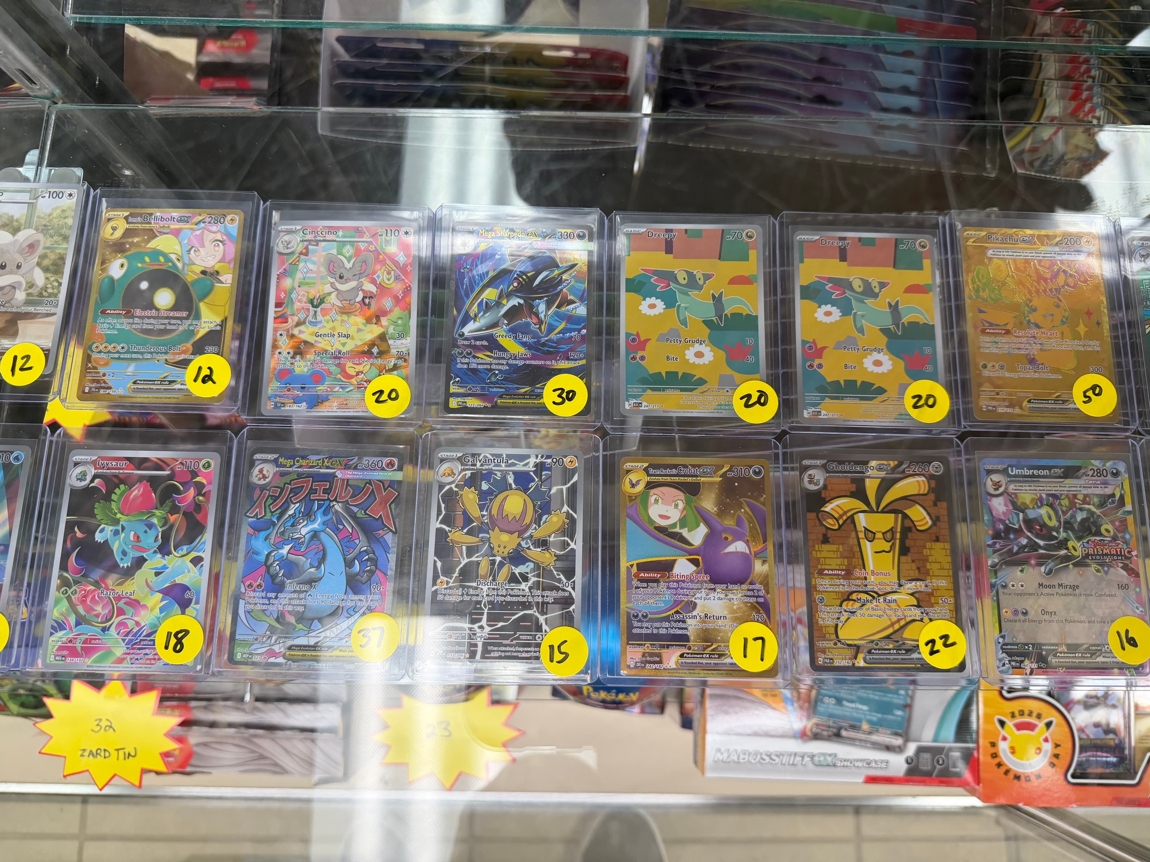 Various Pokémon trading cards in a glass display case with yellow price stickers.
